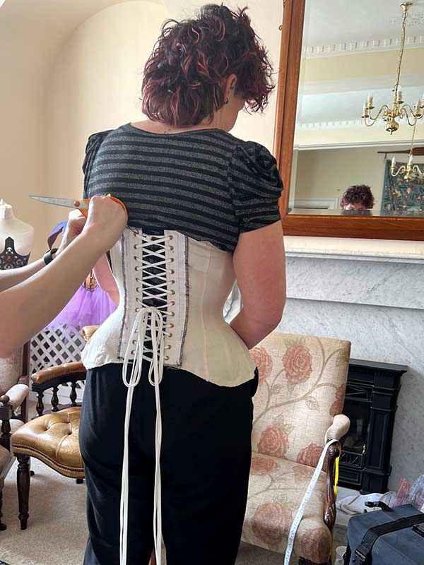 Drea at the March 2023 Corsetry Retreat. They are having alterations done to their mock-up while they are wearing it.