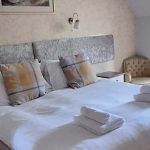 A photograph of a bedroom with large double bed with white bedding and 2 towels rolled up at the foot of the bed the walls are cream with a grey headboard and a picture hanging above the bed.